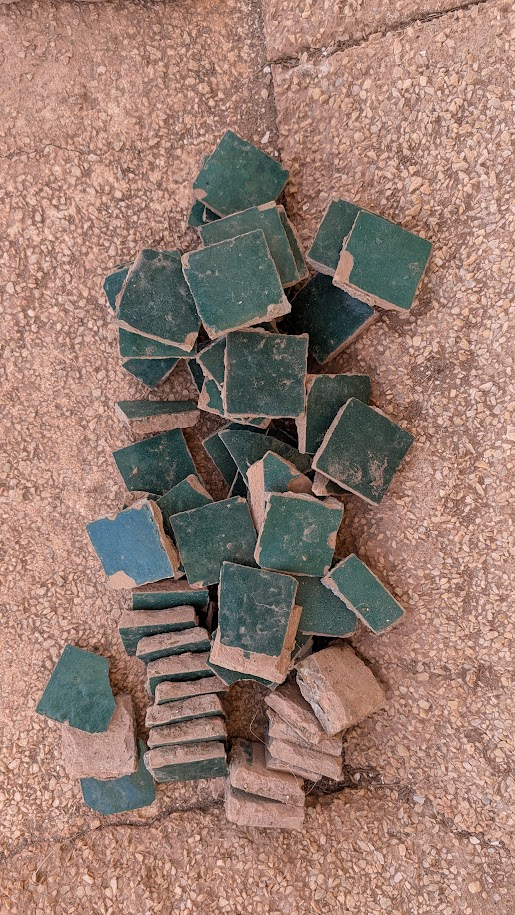 Collected green zellige fragments with exposed clay edges on a tiled surface