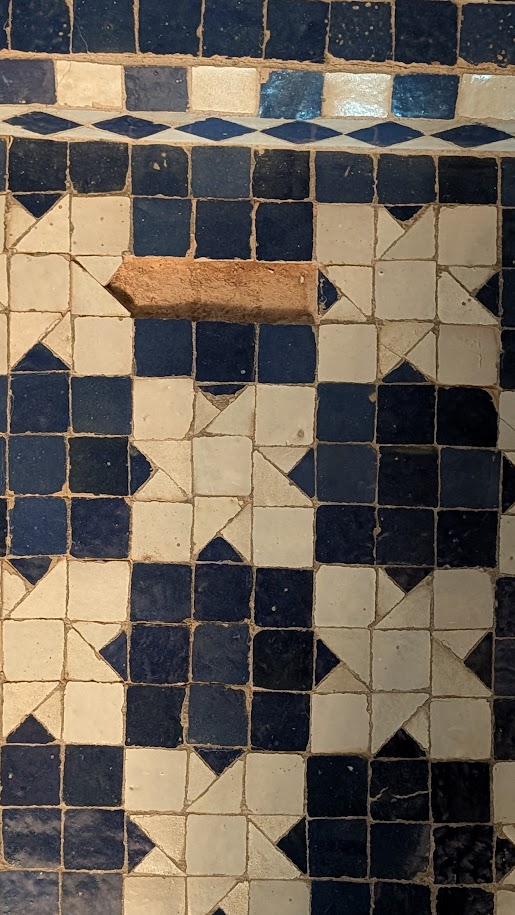 Photographic reference of worn blue and white glazed zellige with visible grout and cracks